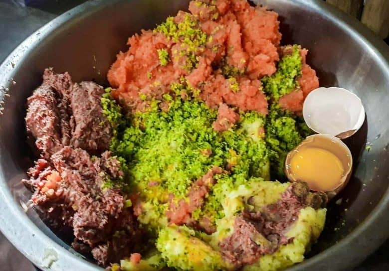 Ground meats with vegetables and raw egg on a metal bowl