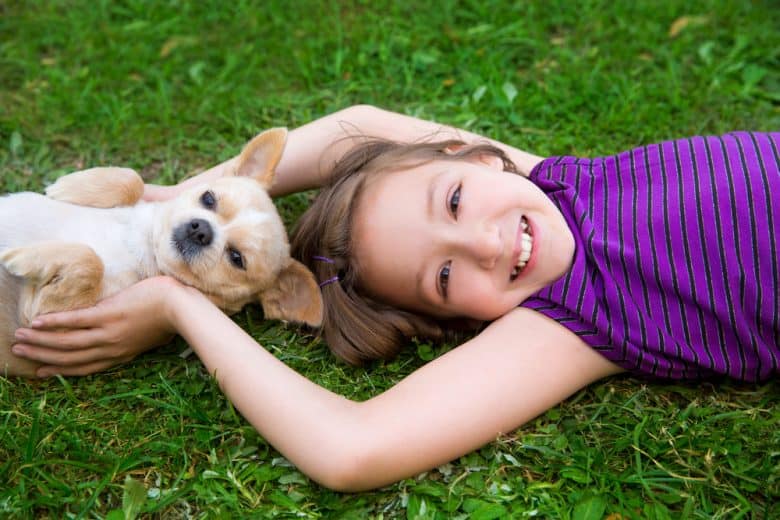 A girl laying on the grass with a Chihuahua