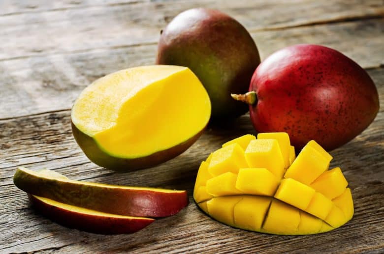 Whole and sliced mangoes in a wooden board