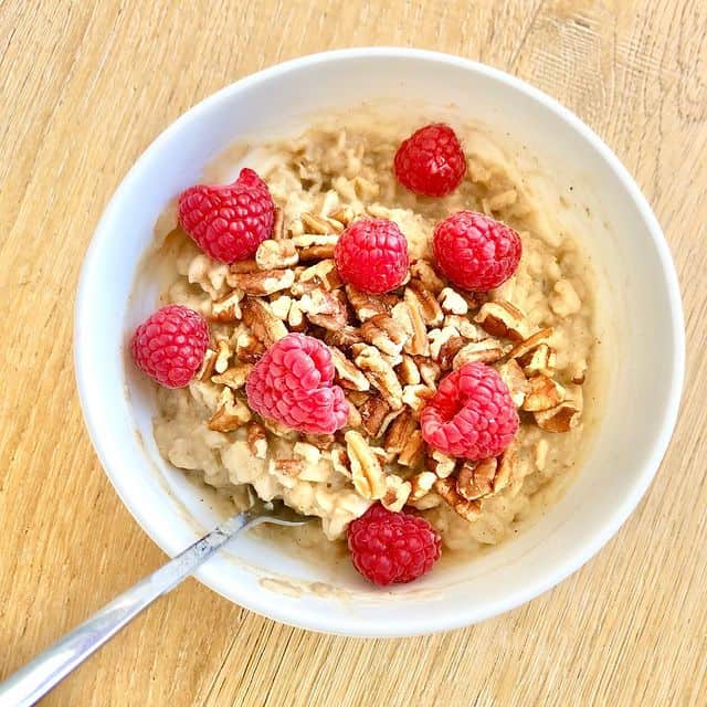 A bowl of cardamom oatmeal with raspberries and pecans