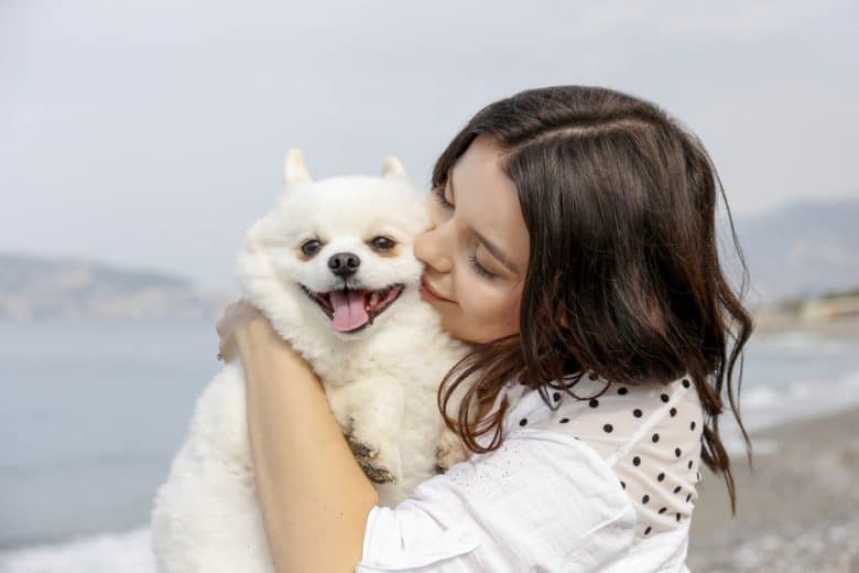 A woman carrying and hugging a white Pomeranian dog